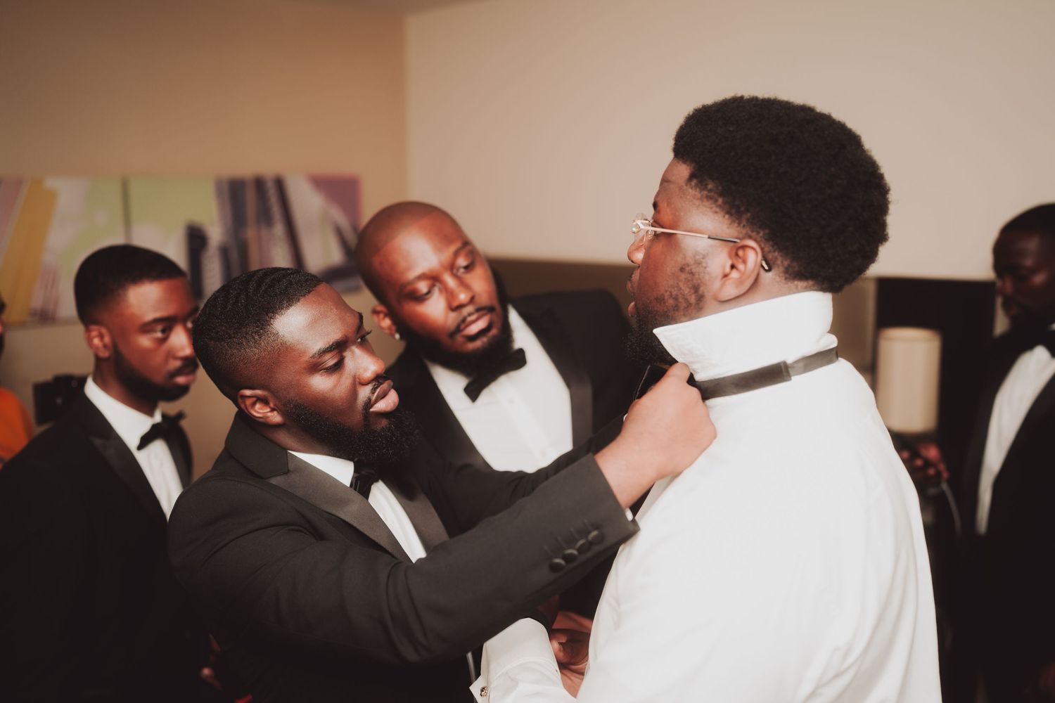 Groomsmen in formal black tuxedos share a lighthearted moment during wedding preparations.