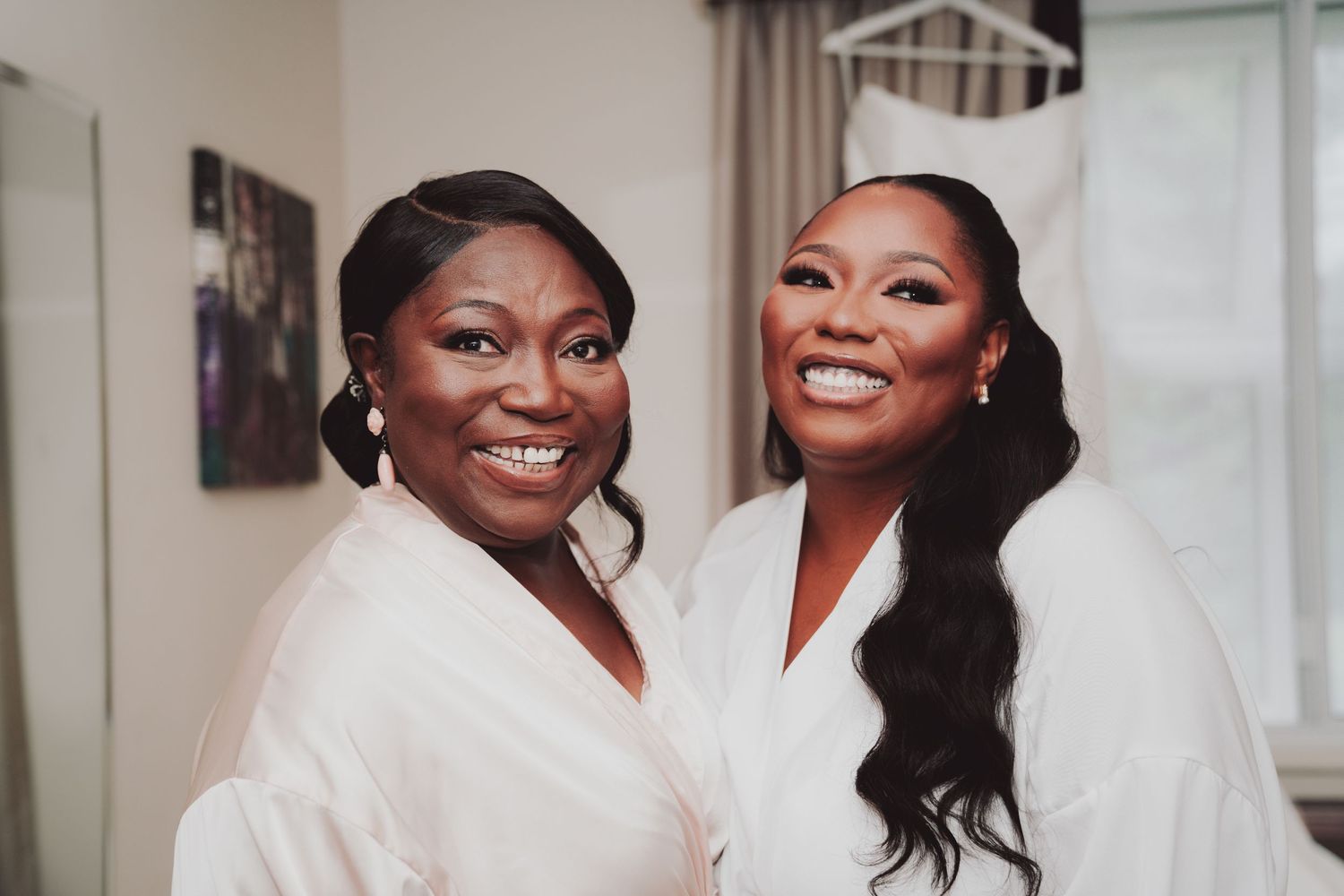 Two people in white robes sharing a joyful moment during wedding preparations.