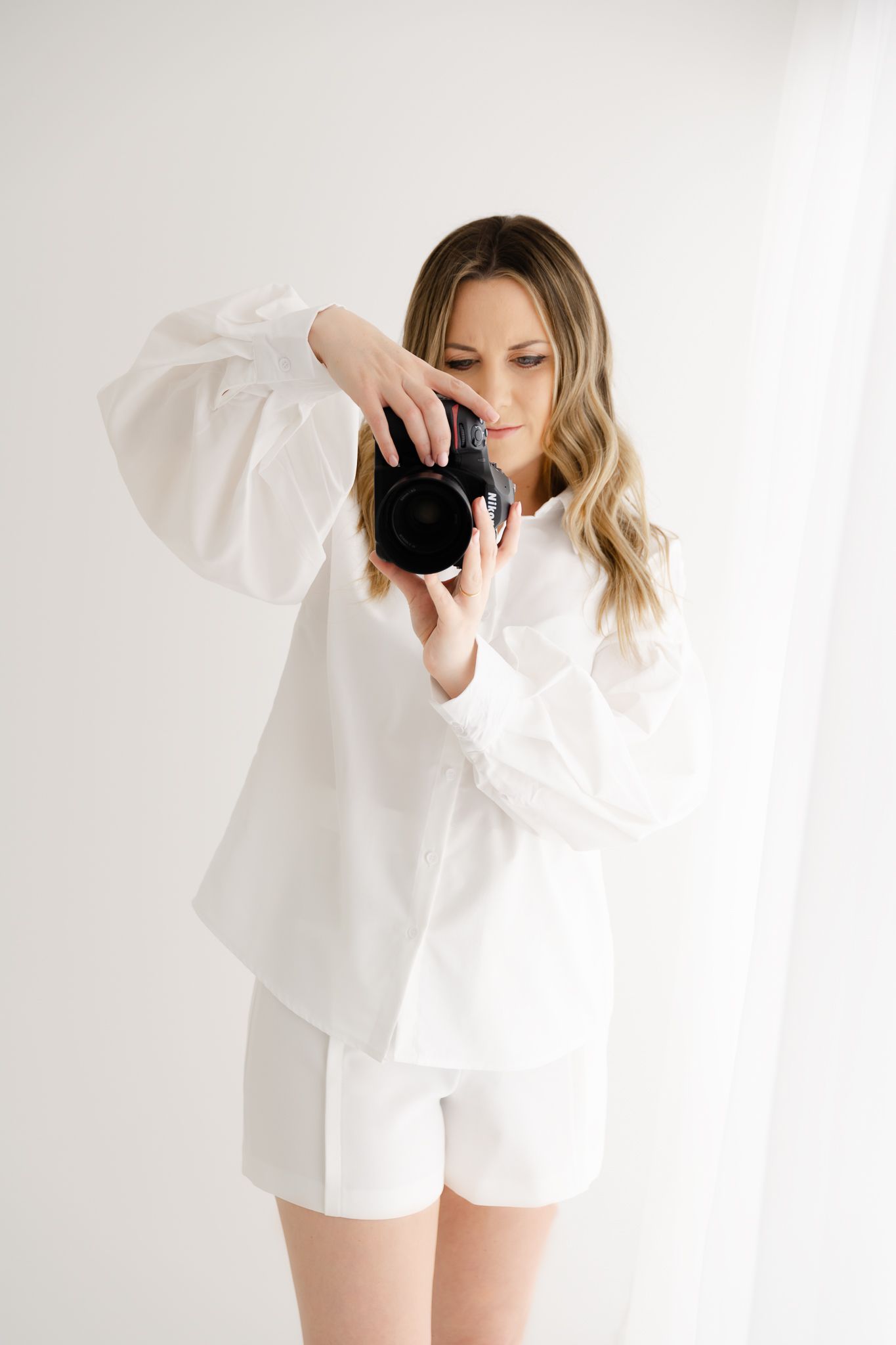 Photographer in white outfit holding camera against minimal light background.
