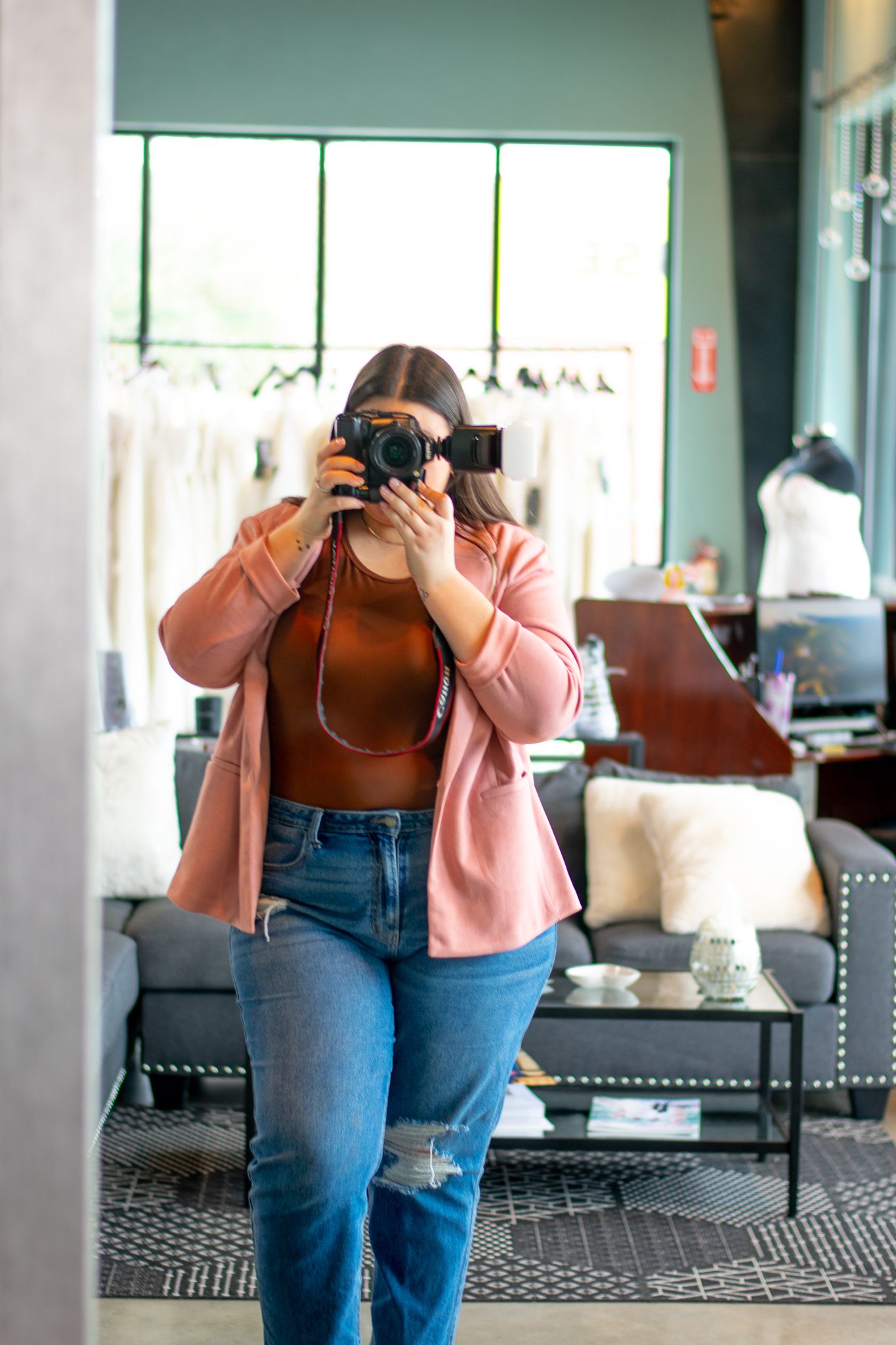 A photographer in a pink cardigan and jeans takes photos with a professional camera in an indoor setting.