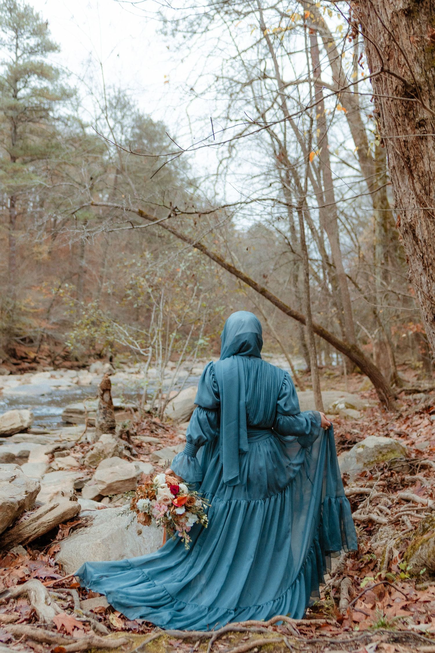 A dramatic photo of blue flowing dress against rocky forest landscape.