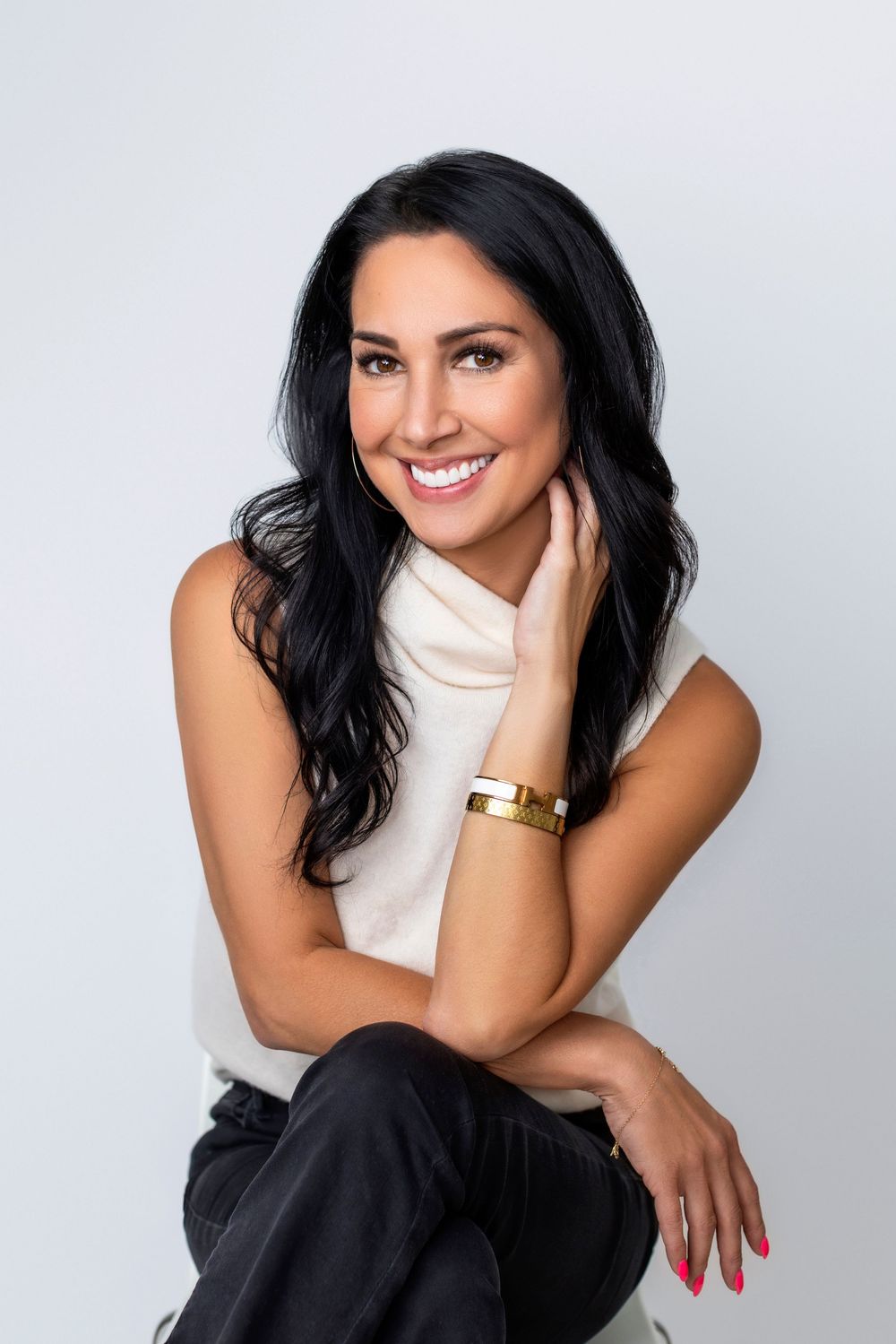Professional studio portrait of someone wearing a white turtleneck and dark pants in elegant poses against light background.