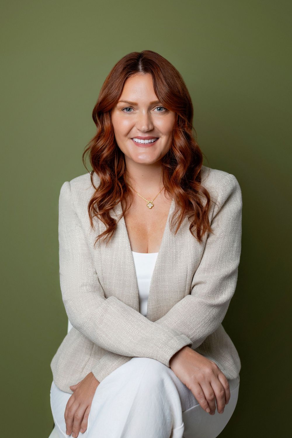 Professional portrait of someone in a light beige blazer and white top against a green background.