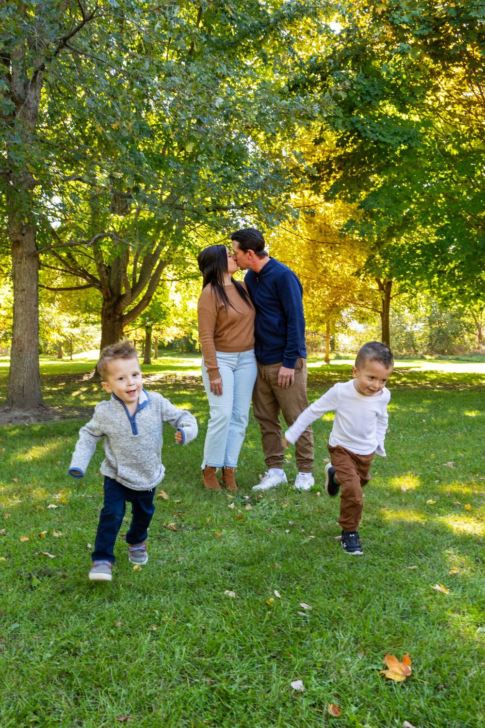 A family of mom, dad and 2 boys. Mom and Dad kissing with the two boys running towards the camera
