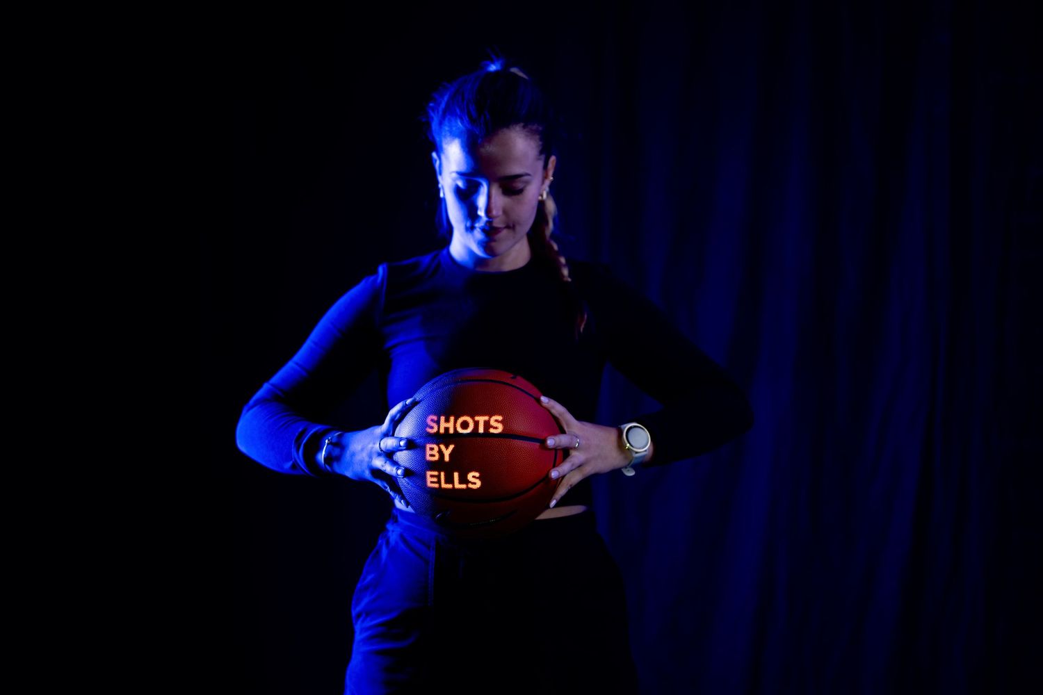 Basketball player poses with ball in dramatic blue lighting for promotional photo.