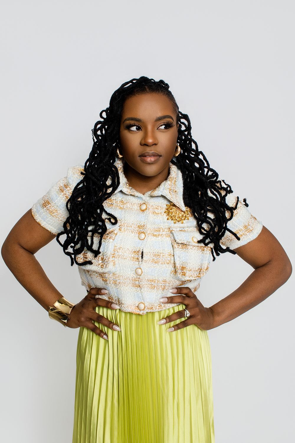 Fashion portrait in a white patterned top and lime green pleated skirt against white background.