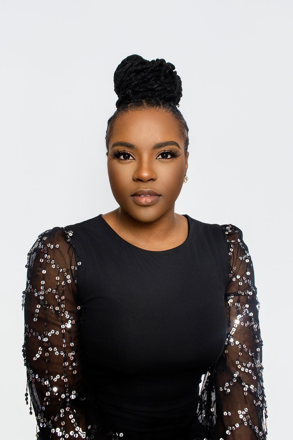 Elegant portrait in black dress with sheer sequined sleeves against white background.