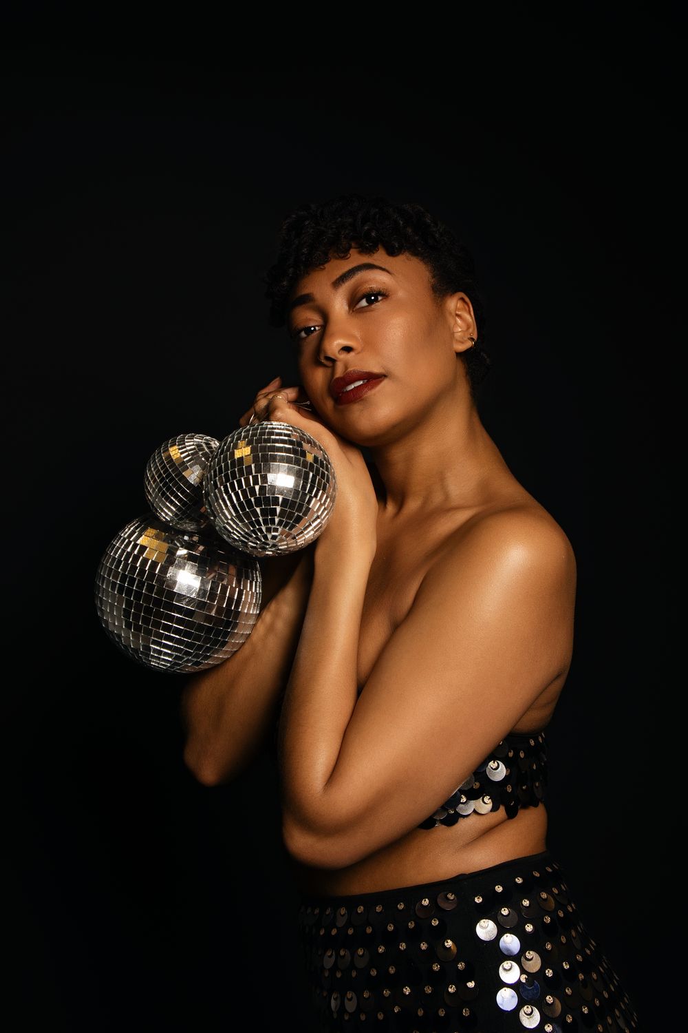 Low-key portrait featuring disco ball and sequined dress in dark setting.