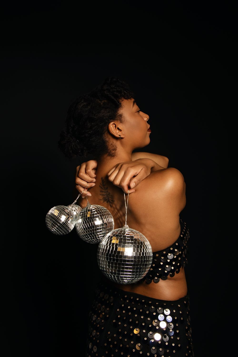 Artistic pose with disco ball and sequined outfit in moody lighting.