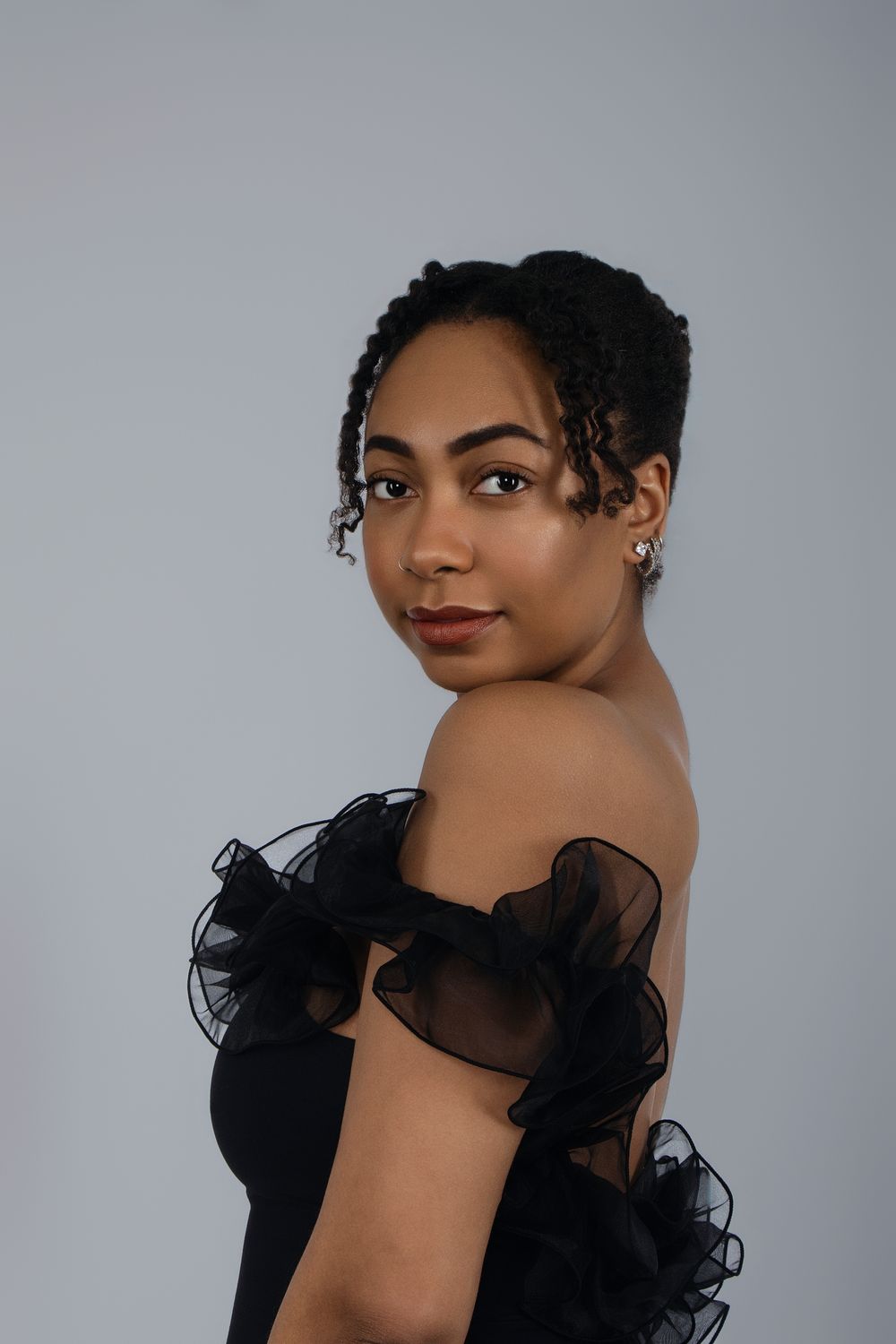 Figure in black tulle top poses elegantly against grey backdrop.