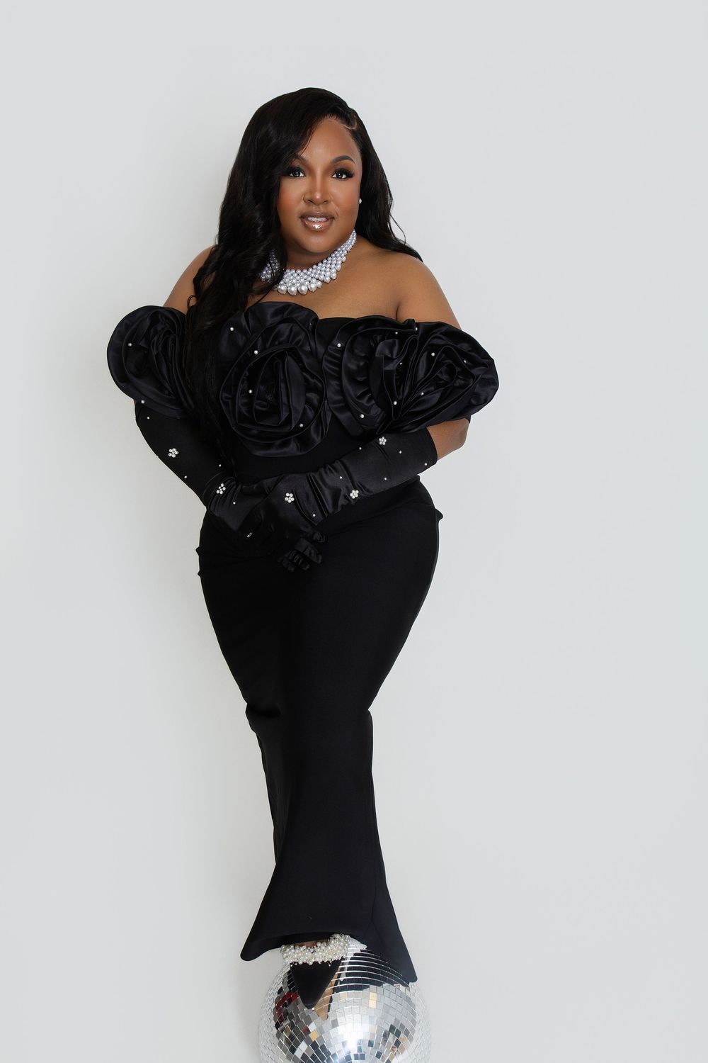An elegant pose in a black off-shoulder dress with a disco ball prop.