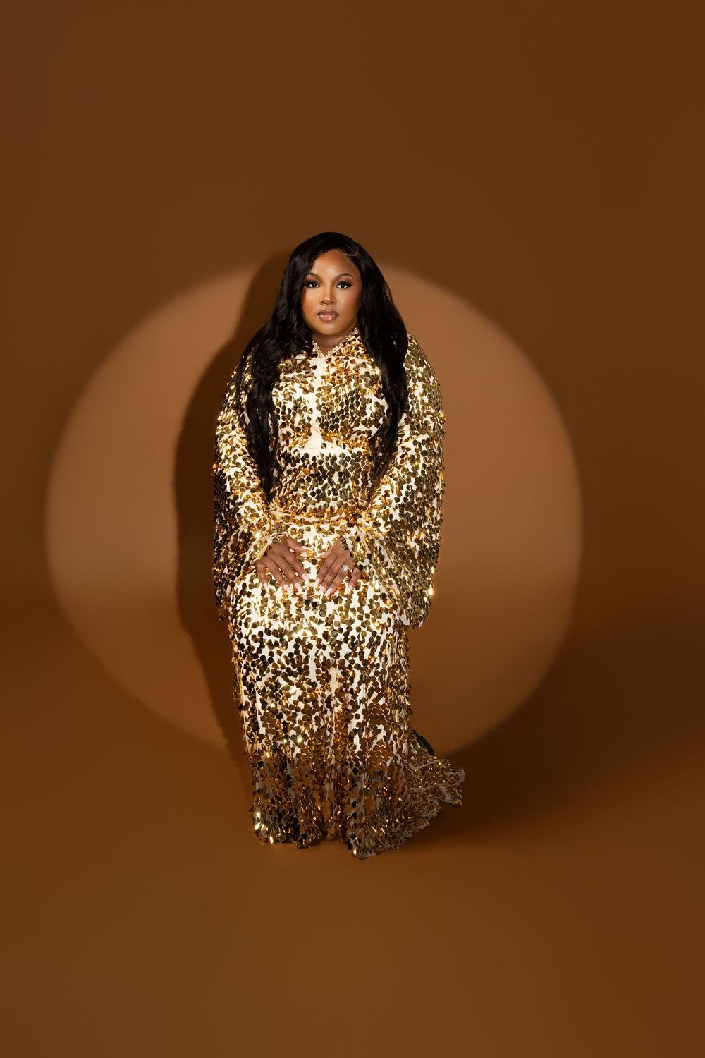 A glamorous fashion photo featuring a gold sequined gown against a brown backdrop.