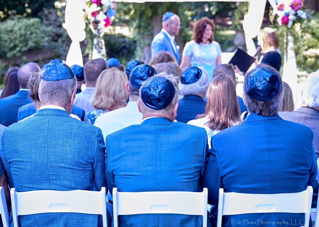 Jewish men in blue suits wearing blue Yamakas at Jewish wedding in Woodinville, WA at winery.  Bride and groom are in the background.