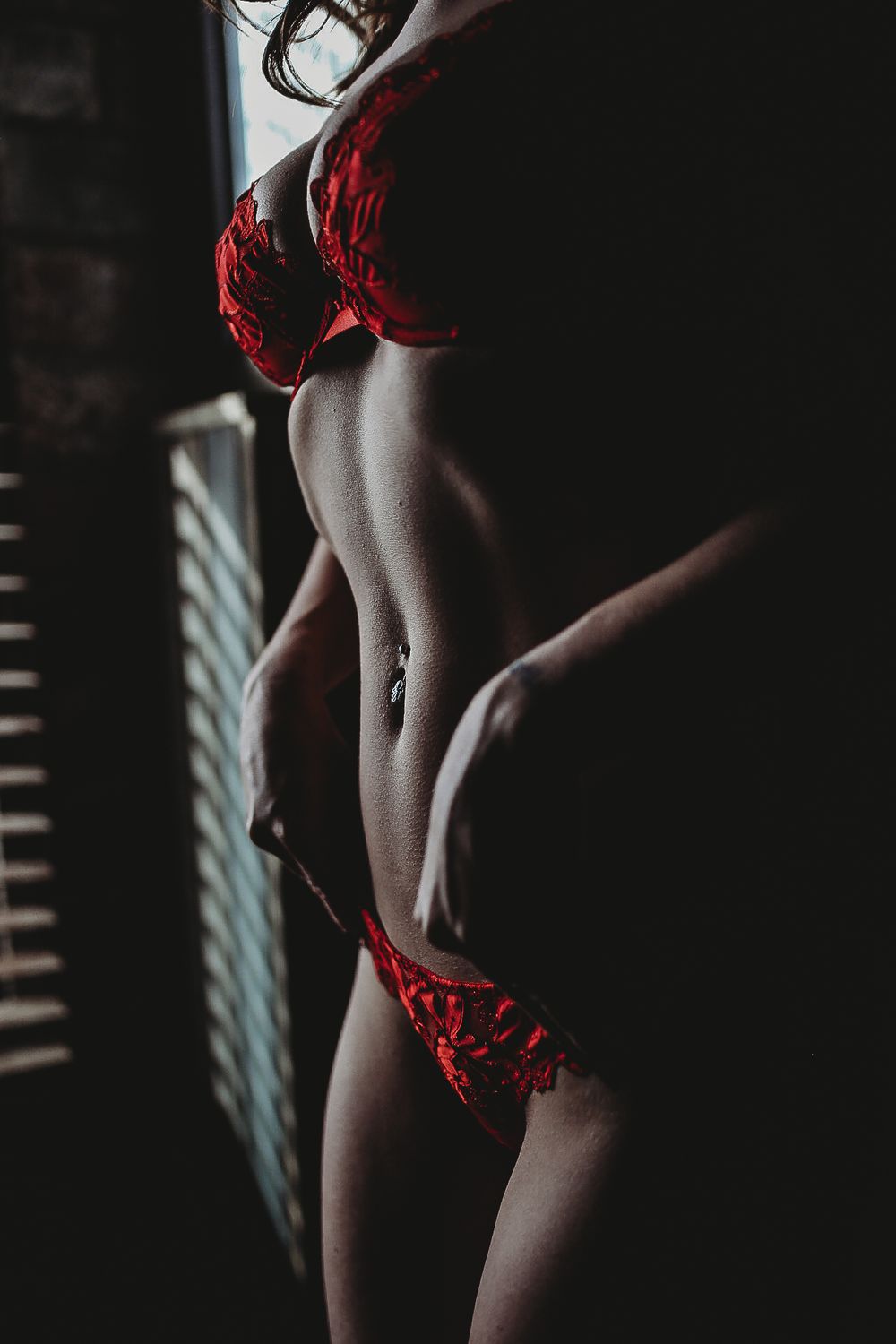 Artistic boudoir photoshoot series showing woman in red lingerie against dark background with window light.