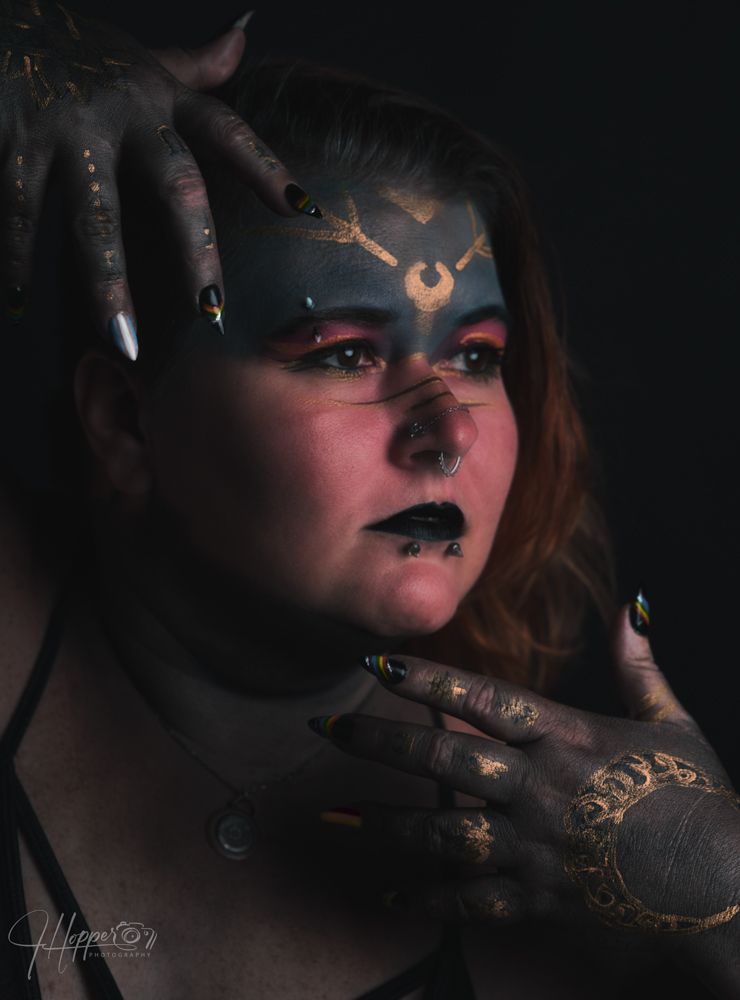 Dark artistic portrait with dramatic lighting showcases gold glitter makeup and black lipstick in a moody atmosphere.