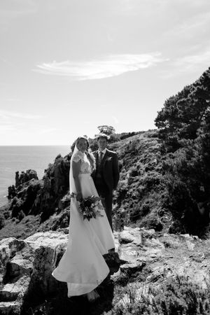 A couple poses together on dramatic coastal cliffs overlooking the ocean.