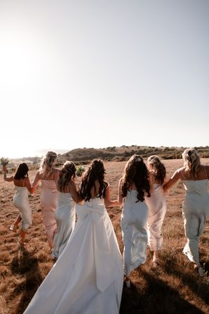 A group of people in white dresses dance together in a line against a desert landscape at sunset.