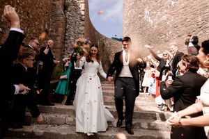 Newlywed couple walking down stone steps while guests throw colorful confetti at their outdoor wedding celebration.