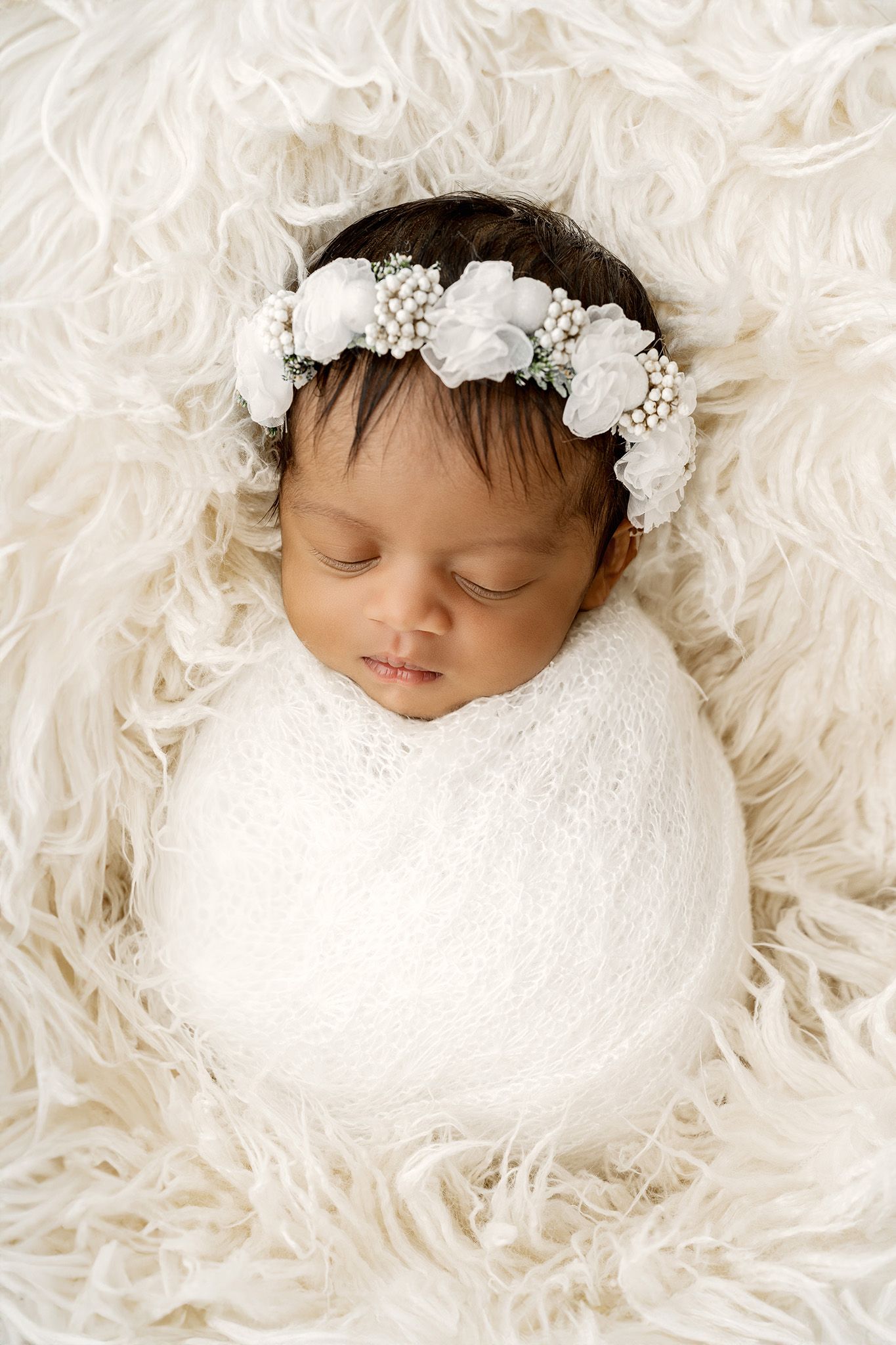 Newborn baby on white flokati during newborn session in studio with floral headband