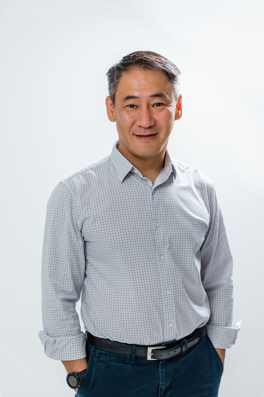 Professional wearing a checkered grey button-down shirt and dark jeans poses against white background.