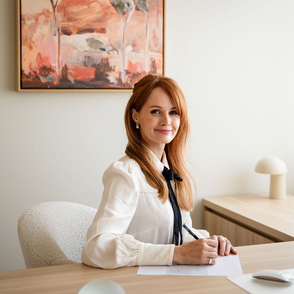 Person in business attire sitting at desk with documents and laptop in modern office setting.