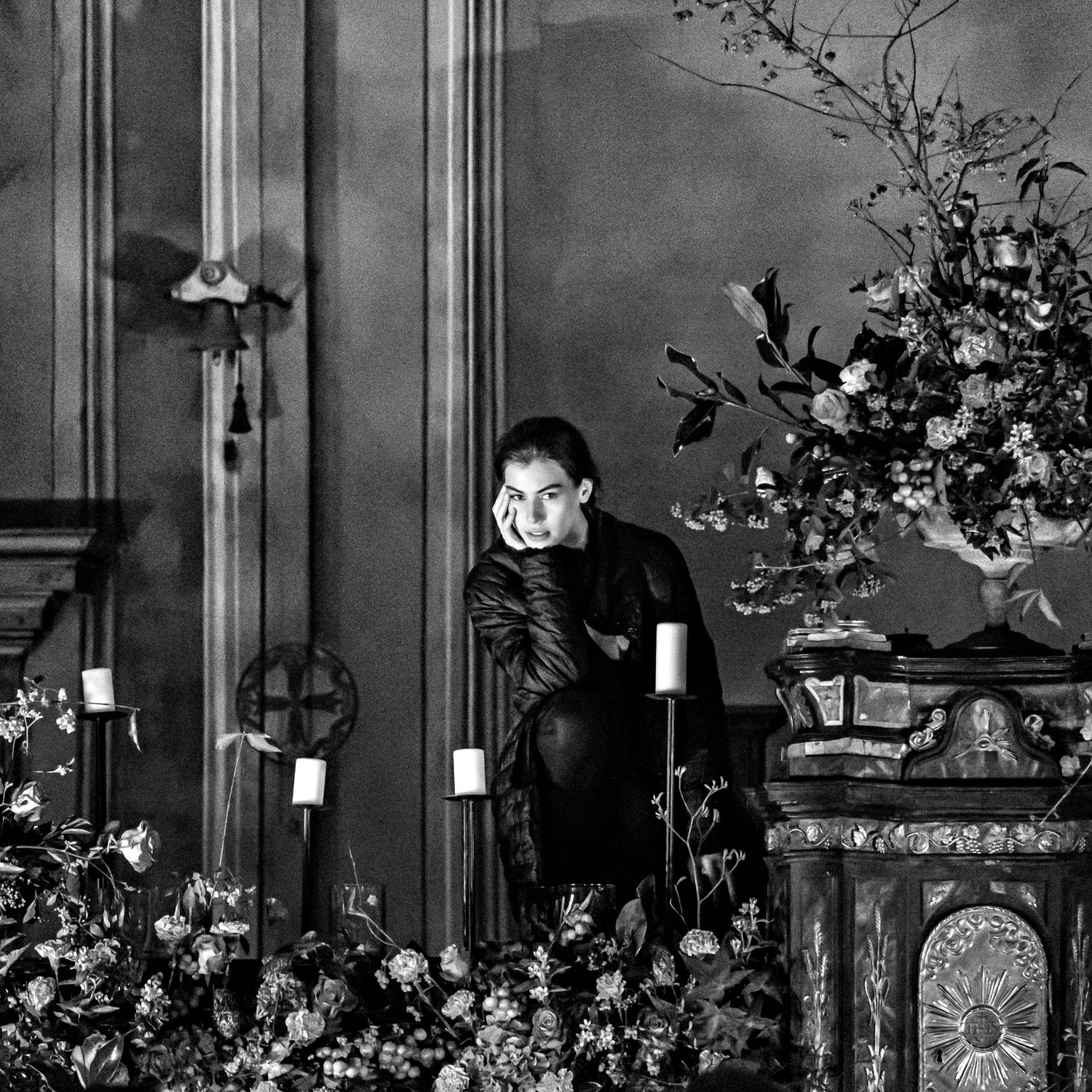 Una fotografia di ritratto artistico in bianco e nero che mostra una scena interna scura con candele ed elementi decorativi.