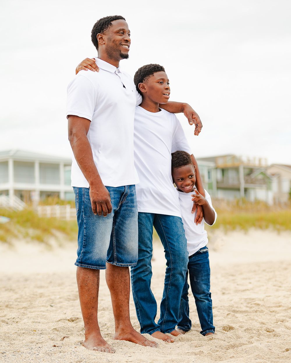 Three people in white shirts and jeans standing together on beach.
