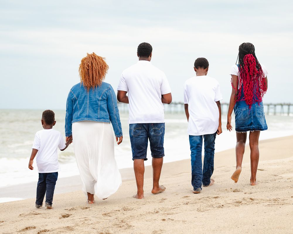 Family walking away from camera along beach shoreline in casual wear.