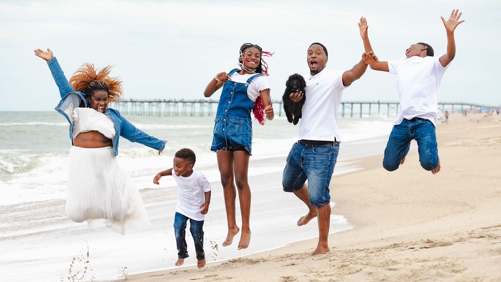 Family jumping and celebrating together on beach with pier in background.