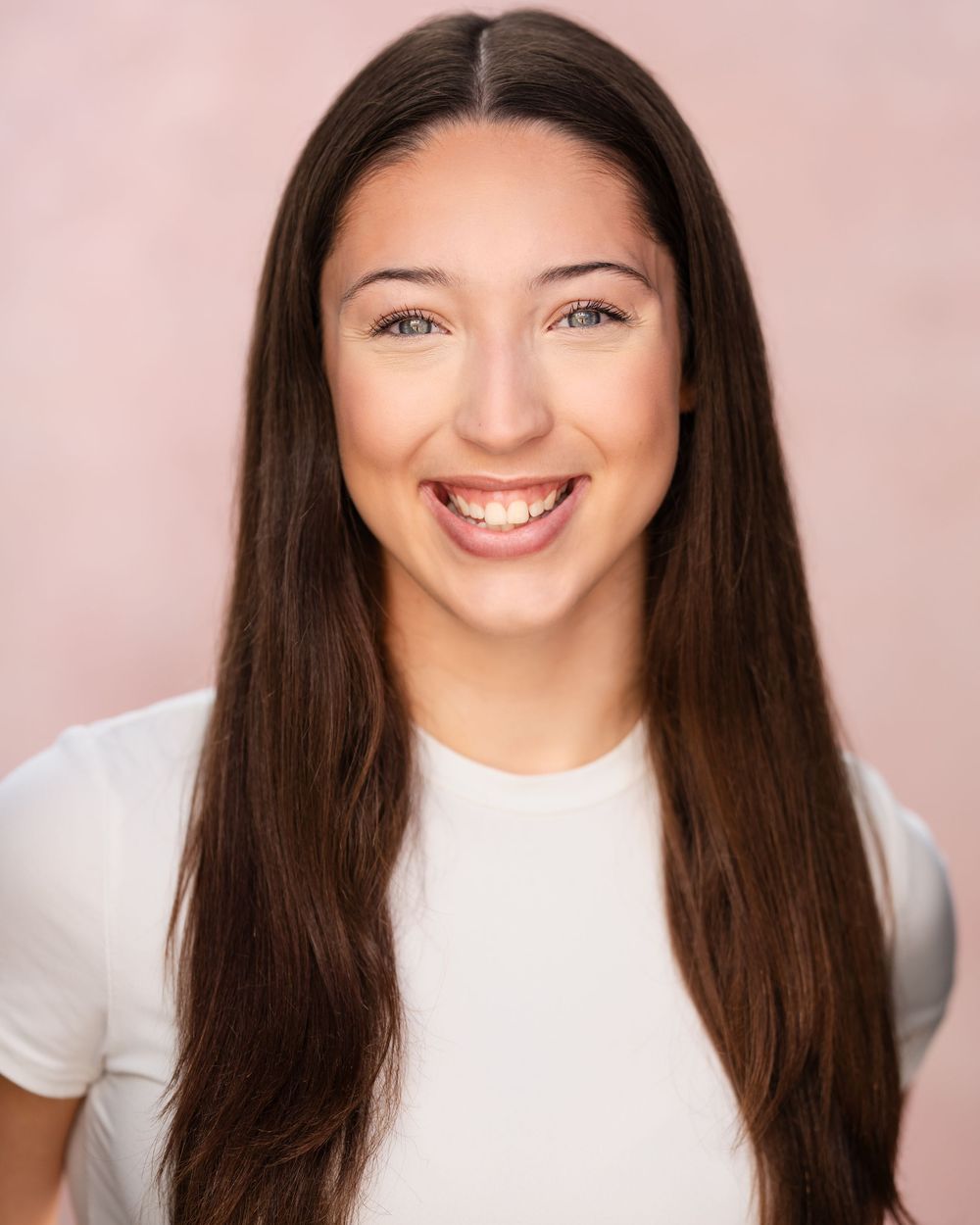 Headshot series showing expressions transitioning from subtle to joyful smile in white top against pink backdrop.