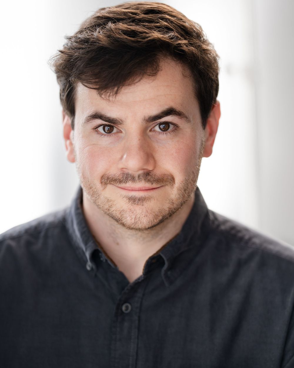 Professional headshot of someone in a dark shirt against a light background showing a warm smile.