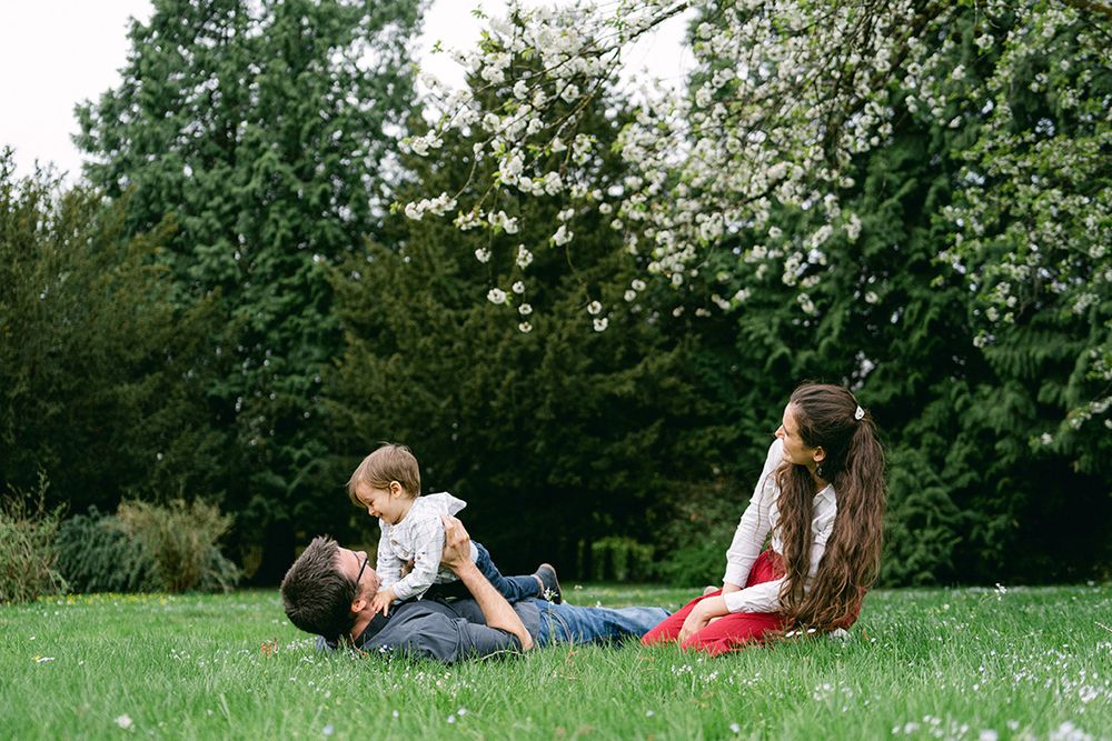 A family enjoys a playful moment together on lush grass under blooming trees.