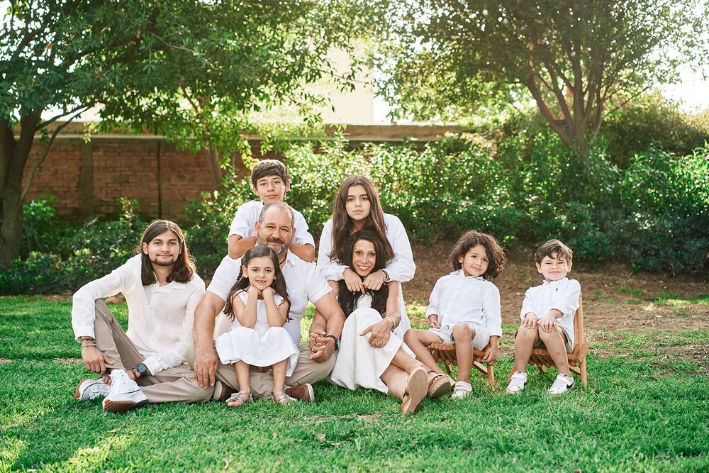 Group photo of people wearing white clothes sitting together on grass in a garden setting.