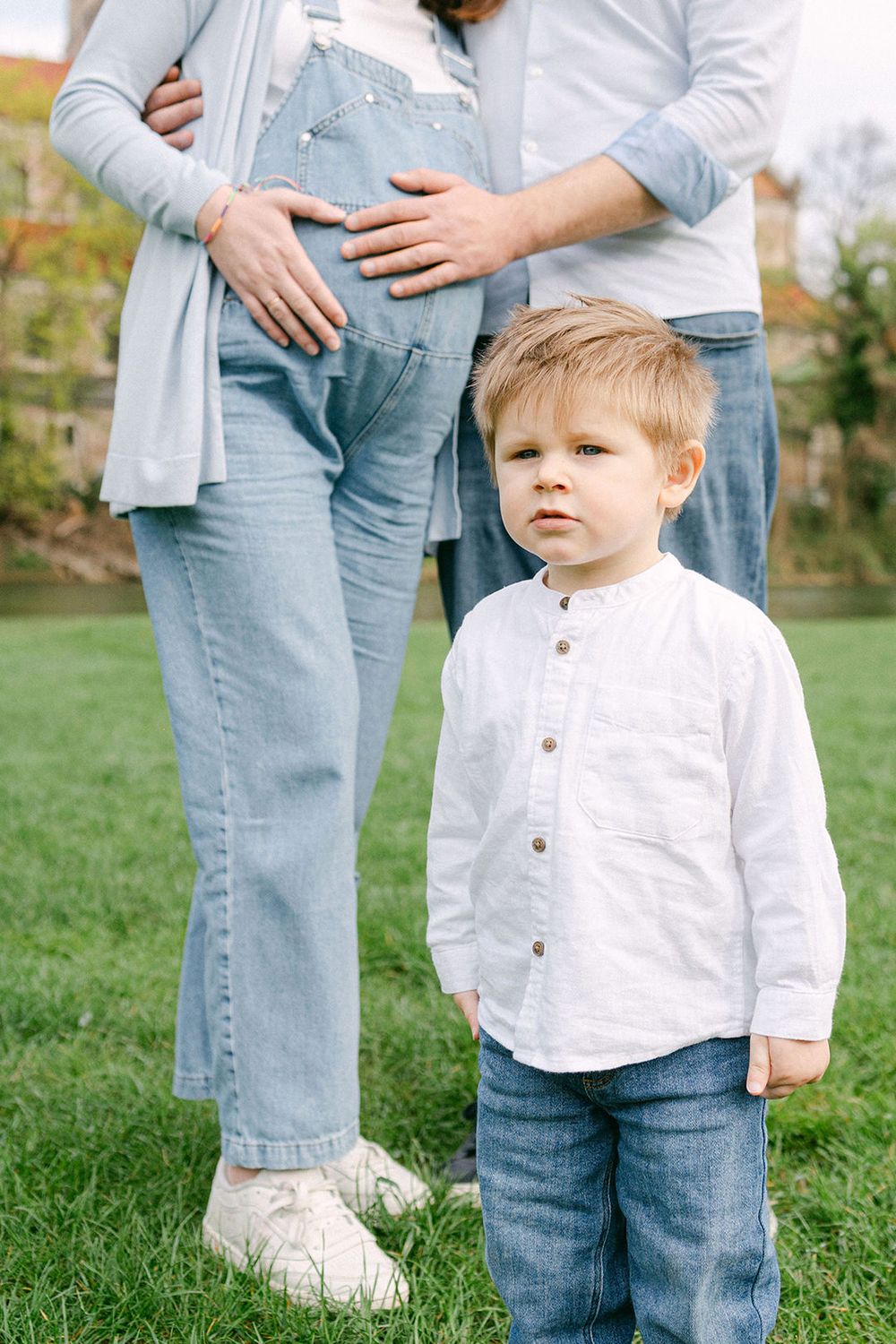 Child in white shirt standing in front of people in casual denim outfits on grass.