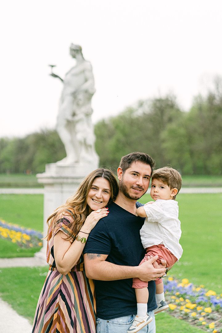 A family poses together in a garden with a classical statue visible in the background.