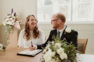 A couple signs wedding documents at a table decorated with floral arrangements.