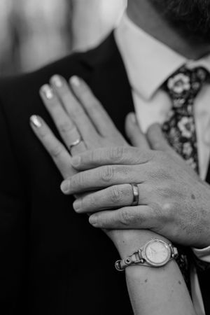 Close-up black and white photo of hands with wedding rings and a wristwatch.