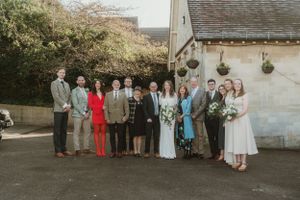 Wedding party poses together outside a church building on a sunny day.