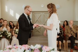 Intimate wedding ceremony exchange of rings in light-filled room with pink floral decor.