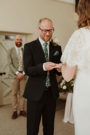 Wedding ceremony moment showing ring exchange in an indoor setting.