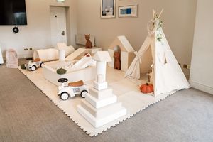 A white teepee tent with cushions and pillows creates a cozy reading nook in a carpeted room.
