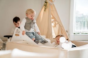 Children play and crawl together on a white carpeted floor in a bright, modern playroom setting.