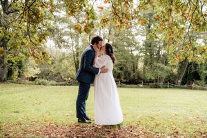 A romantic couple embraces under autumn trees in a park during their wedding photoshoot.