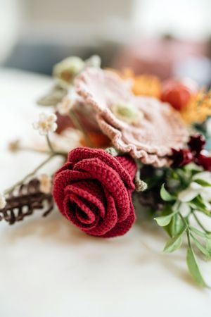A close-up view of delicate red fabric roses with green foliage accents arranged in a soft, dreamy composition.
