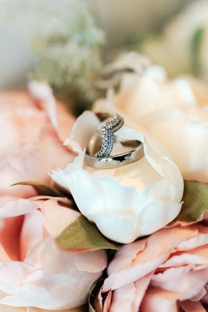Wedding rings nestled in white peony bloom surrounded by blush pink roses in a romantic bridal bouquet arrangement.