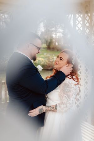 A bride and groom share a tender moment framed by a lattice gazebo, the groom gently cupping the bride's face.