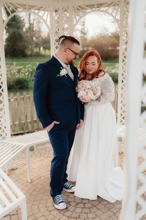 Bride and groom share a tender moment under a white gazebo, bride holding a pink bouquet in a white gown.