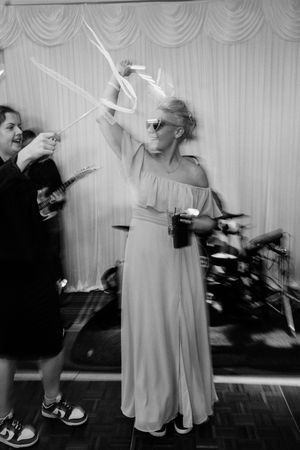Black and white photo of women dancing at a wedding reception, one in a long dress with balloon wands.