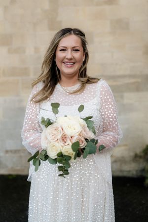 A bride in a white lace dress with polka dots holds a soft pink and white rose bouquet with eucalyptus.