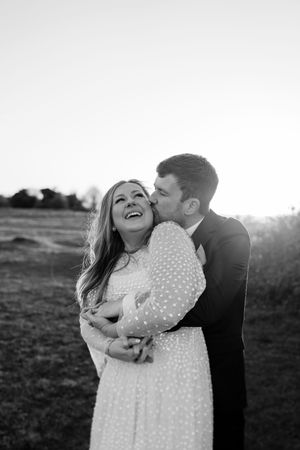 A couple embraces and laughs together in a field during sunset in black and white.